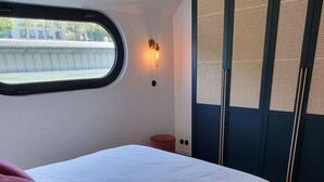 A bedroom with a bed, a window, a plant, and a wall-mounted light fixture.