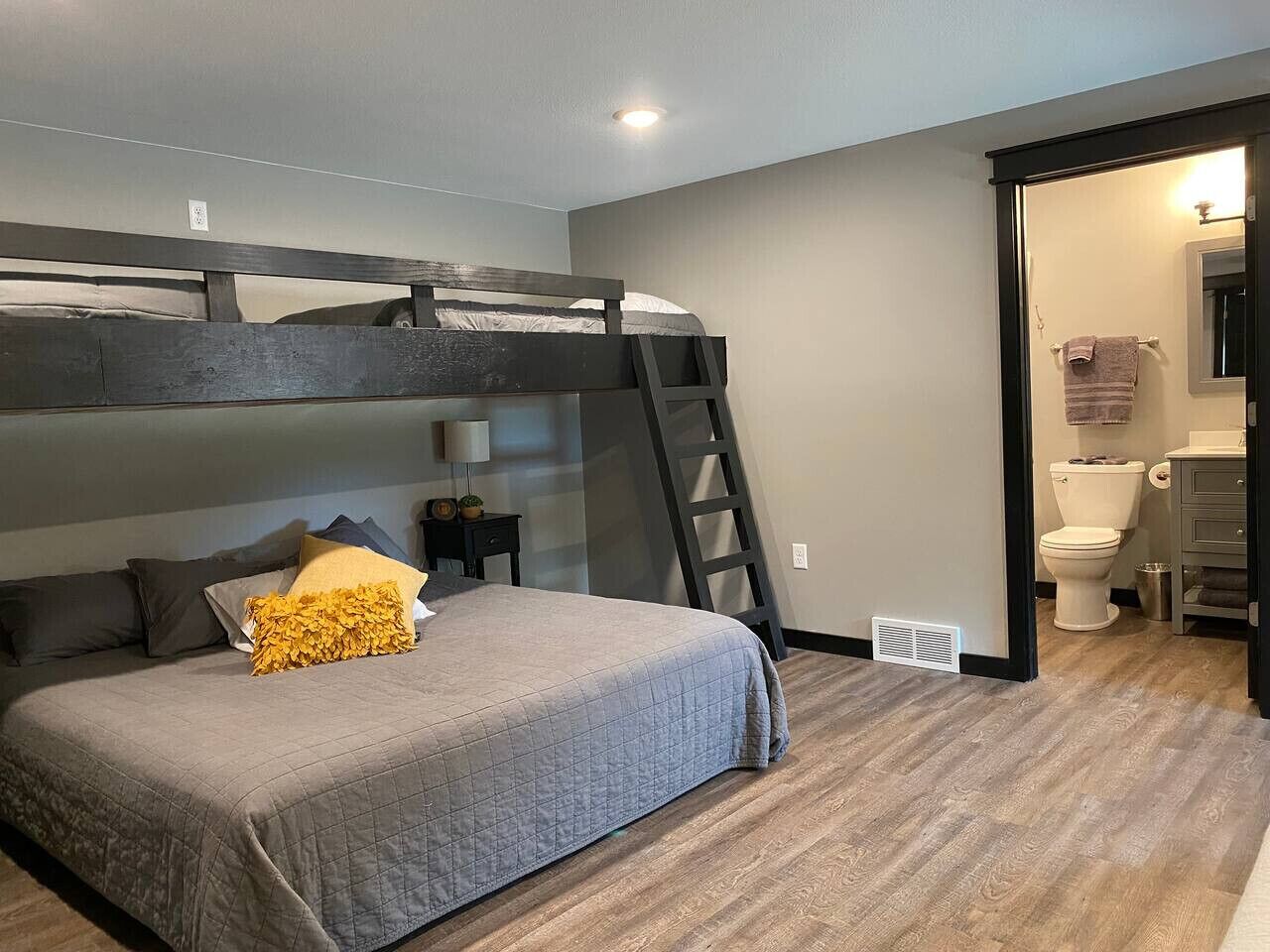 Une chambre avec un lit superposé, une table de chevet avec une lampe, et une salle de bain visible à travers une porte ouverte.