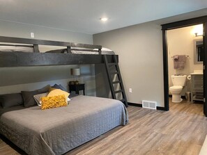 A bedroom with a bunk bed, a bedside table with a lamp, and a bathroom visible through an open door.