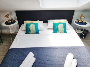 A neatly made bed with two pillows, a blue quilted bedspread, and two bedside lamps on white tables.