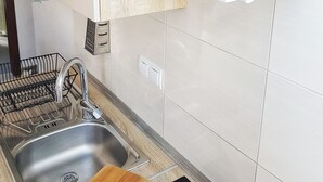 A kitchen with a stainless steel sink, a wooden cutting board, and a white shelf with kitchen utensils and decorative items. - Spectacular View only 5 min. walk from beach, restaurants, attractions and more! (Korčula)
