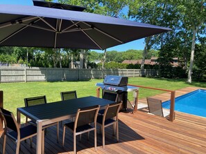A deck with a table and chairs, a grill, and a pool. - Summer in the Hamptons (Westhampton Beach)