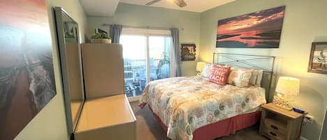 Quarto com cama, ventoinha no teto, mesa de cabeceira com abajur e vista para o exterior através de uma porta de correr.