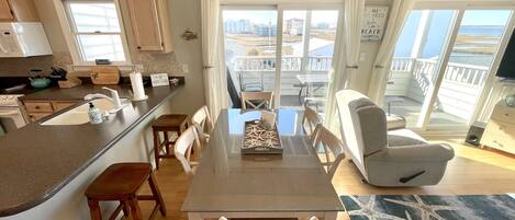 A modern kitchen with a large island, dining area with a table and chairs, and a balcony with a view of the sea.