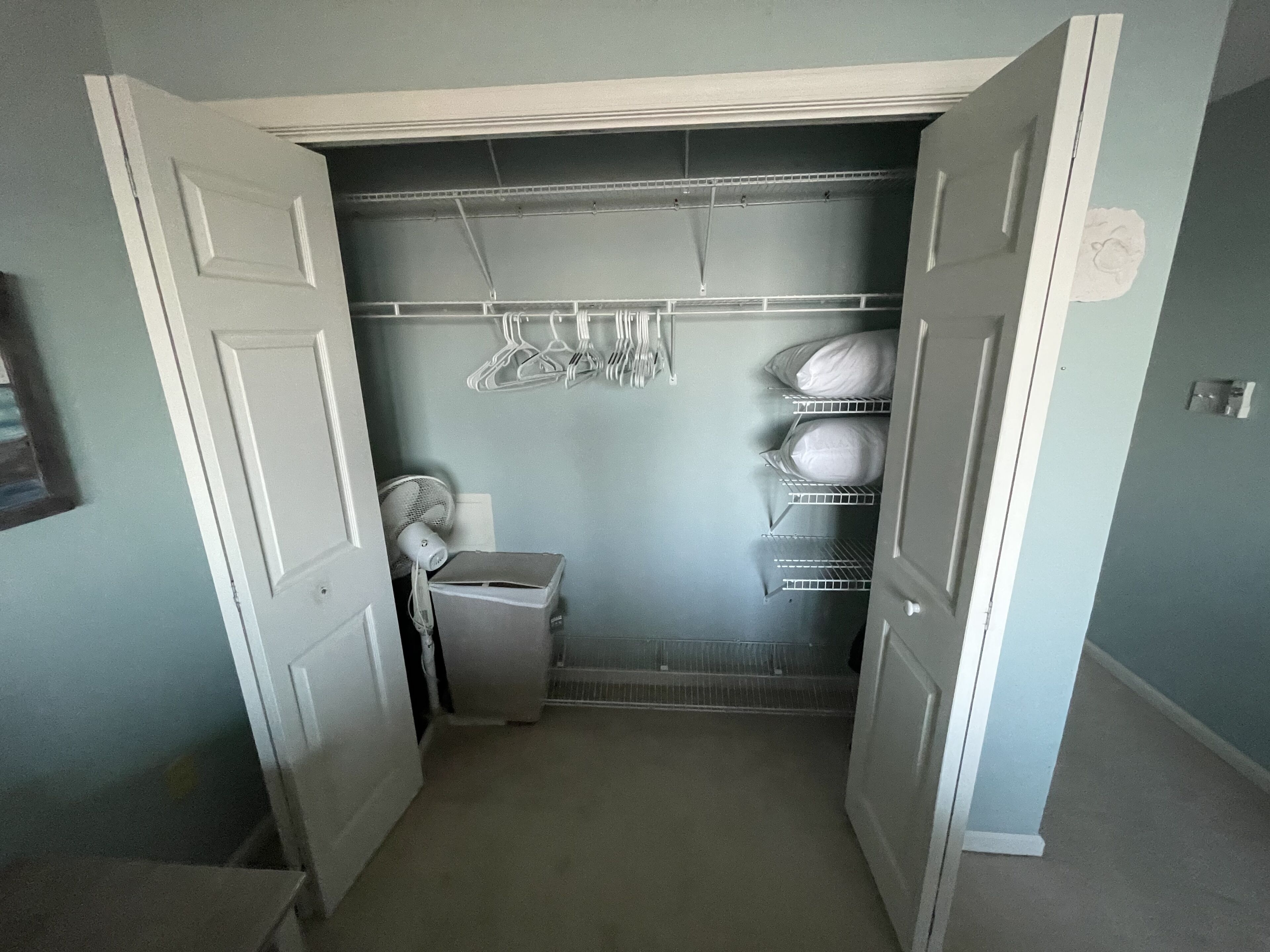 Ein schmaler Flur mit einem Schrank, der Regale, einen Ventilator und Kleiderstangen enthält.