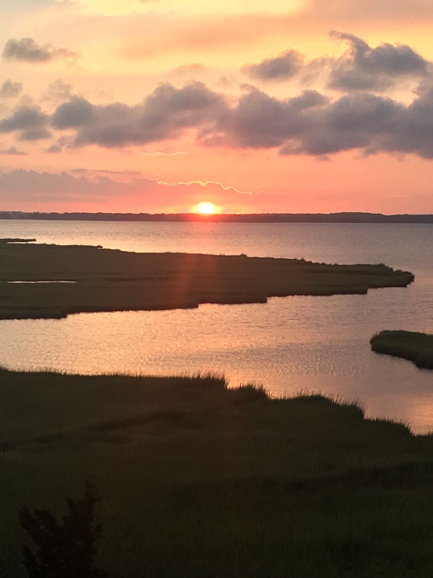 A sunset over a calm body of water with a distant shoreline.