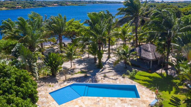 Zona de piscina con vista despejada al mar, rodeada de palmeras y una estructura de techo de paja.