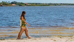 Una mujer caminando por la playa con una masa de agua al fondo.