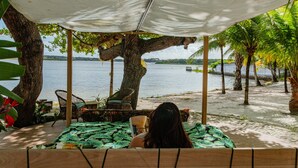 Un espacio de estar junto a la playa con vista al agua, rodeado de árboles y una pérgola.