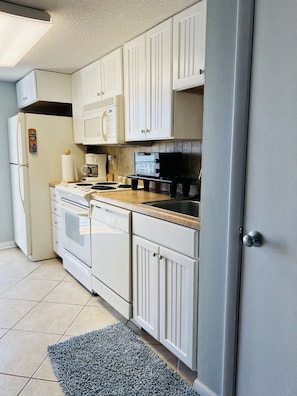 Kitchen area with a refrigerator, stove, microwave, and coffee maker.