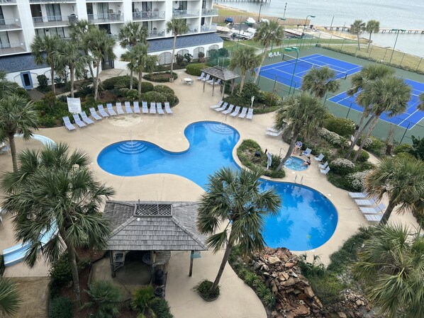 Relax by the resort's wave-like pool, surrounded by lounge chairs and a gazebo, with a scenic view of the nearby water.