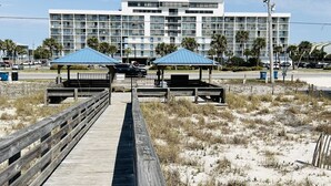 Un hotel frente a la playa con un paseo marítimo de madera que conduce a zonas de estar cubiertas y un edificio moderno con varios balcones.