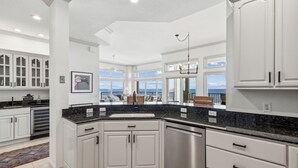 Een moderne keuken met witte kastjes, een RVS vaatwasser en een groot raam met uitzicht op de oceaan.
