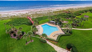 Een resort met een zwembad, palmbomen en uitzicht op het strand.