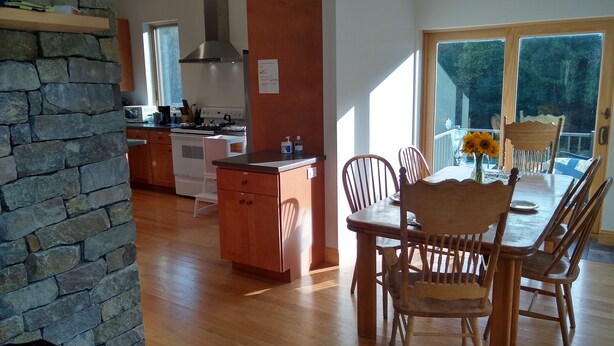 A modern kitchen with a stone accent wall, wooden cabinets, and a dining area with a large table and chairs. - Large relaxing house in 25 acres of private woods with lake access. (Spencer)