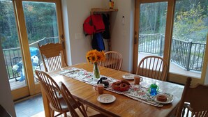 A dining area with a wooden table, chairs, and a view of a balcony with a railing. - Large relaxing house in 25 acres of private woods with lake access. (Spencer)
