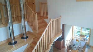 A wooden staircase with a glass railing, leading to a dining area with a table and chairs. - Large relaxing house in 25 acres of private woods with lake access. (Spencer)