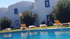 Una piscina con sillas de descanso y un edificio con ventanas de marco azul al fondo.