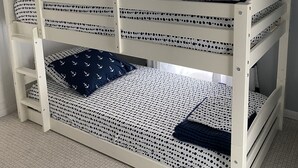 Un lit superposé avec une literie sur le thème de la marine, un ventilateur de plafond, une fenêtre avec des rideaux et un panneau mural sur lequel on peut lire « RELAX ».