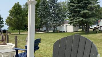 Relax in a serene outdoor space with Adirondack chairs and a table, surrounded by a lush lawn and a majestic evergreen tree.