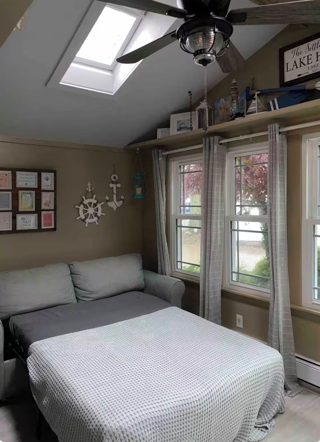 A bedroom with a bed, a ceiling fan, a skylight, and a window with curtains.