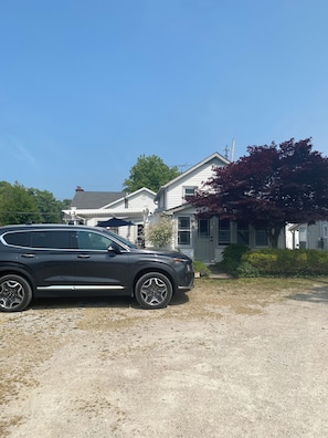 Un SUV negro estacionado en un camino de grava frente a una casa blanca con un árbol de hojas rojas.