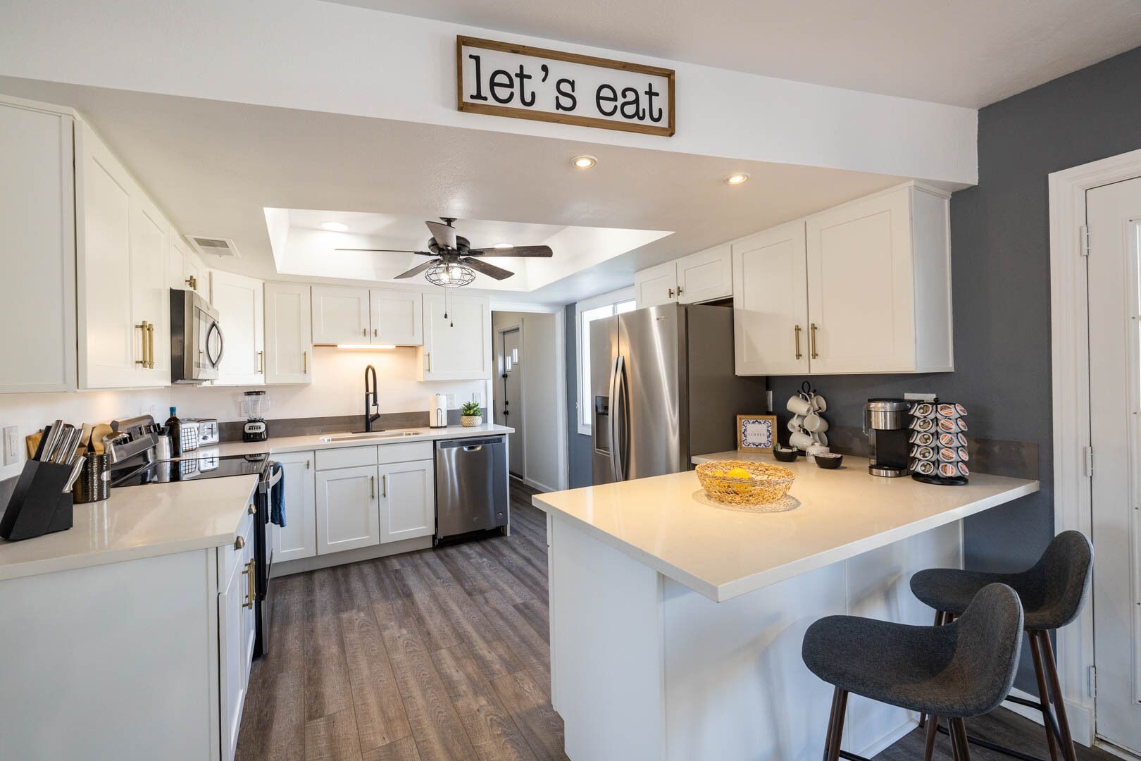 A modern kitchen with white cabinetry, a central island, bar stools, and a ceiling fan.