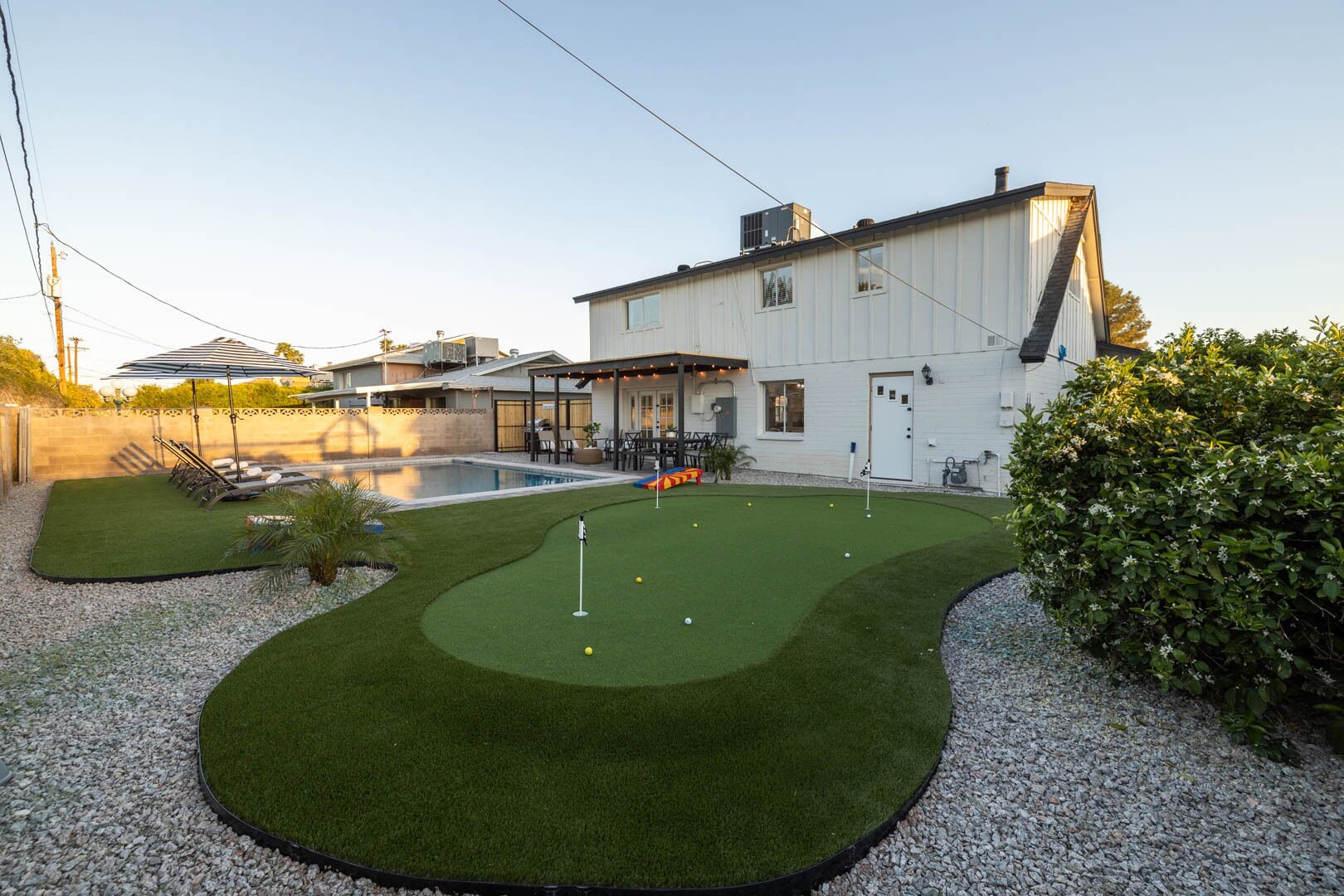 A modern house with a swimming pool, a covered patio, and a well-maintained lawn.