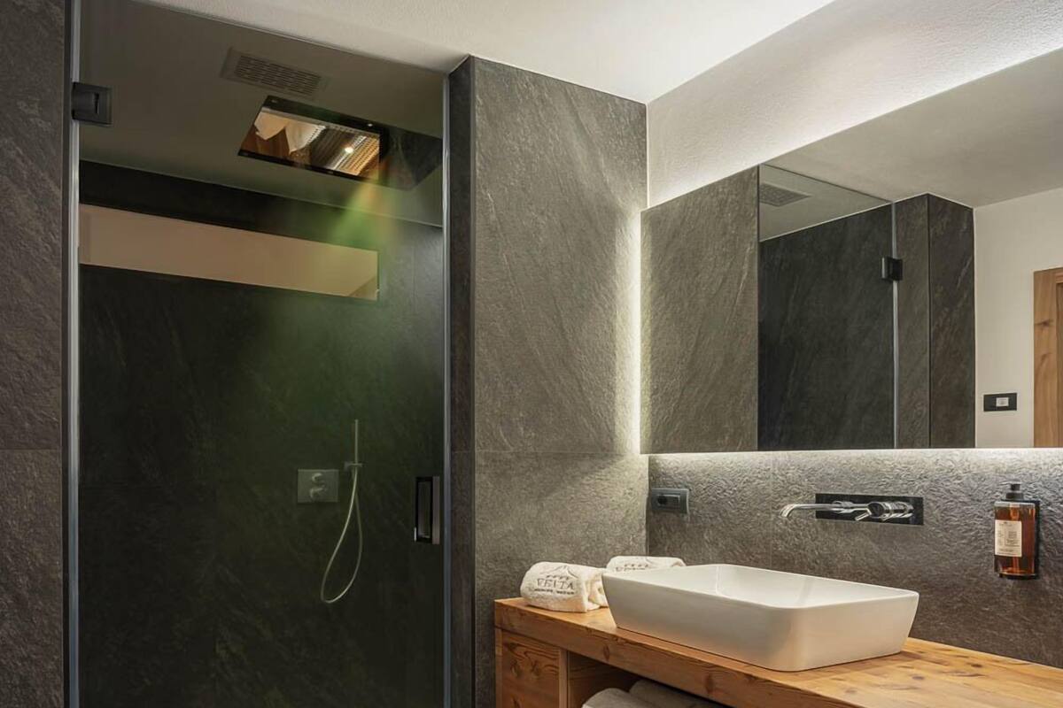 Un baño moderno con cabina de ducha de vidrio, un mueble de tocador de madera con lavamanos blanco y un espejo grande.