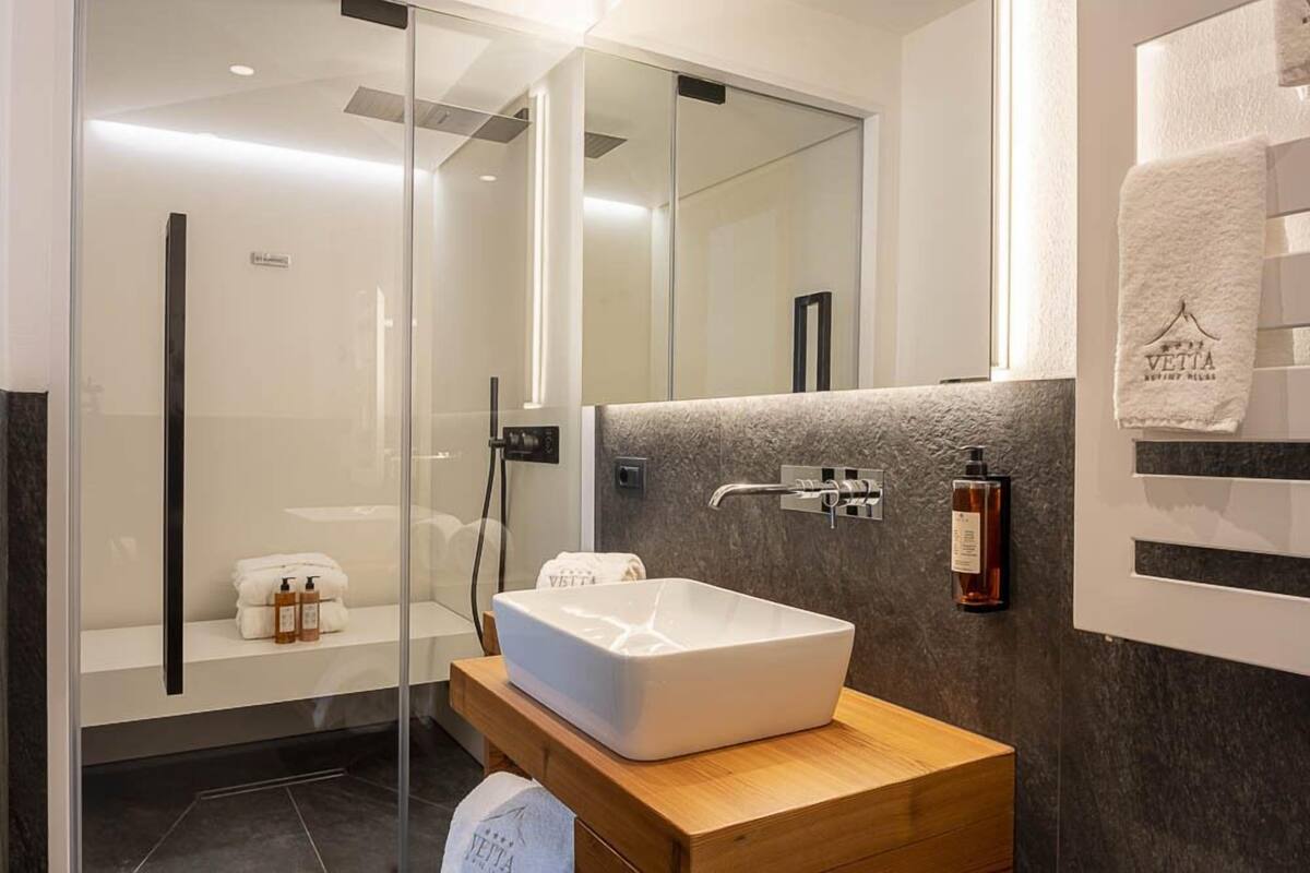Un baño moderno con cabina de ducha de vidrio, un lavabo tipo pedestal blanco y un mueble de tocador de madera.