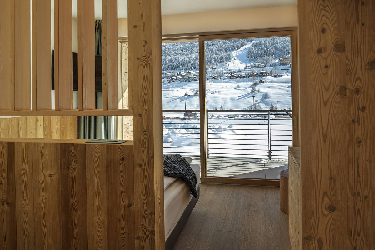 Una habitación de madera con una cama y un ventanal con vistas a un paisaje nevado.