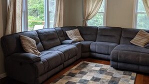 A sectional sofa in a living room with a checkered rug and curtains on the windows. - Lake house 30 minutes from North Conway, NH! (Brownfield)