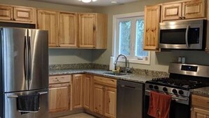 A modern kitchen with wooden cabinets, stainless steel appliances, and a window providing natural light. - Lake house 30 minutes from North Conway, NH! (Brownfield)
