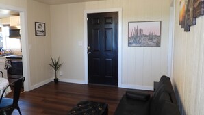 A living room with a black door, a painting of a desert landscape, a potted plant, and a black leather ottoman. - Cozy casita: Bastrop state park view (Bastrop)