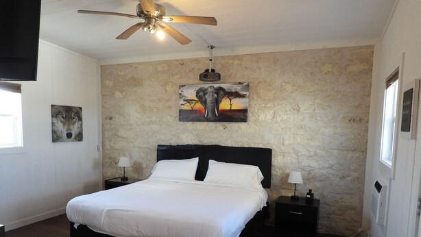 A bedroom with a large bed, a ceiling fan, a painting of a sunset, and a stone wall. - Cozy casita: Bastrop state park view (Bastrop)
