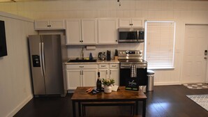 A kitchen with white cabinets, stainless steel appliances, a wooden table, and a bench. - Lovely one room barndominium - The Bastrop Barndo  (Bastrop)