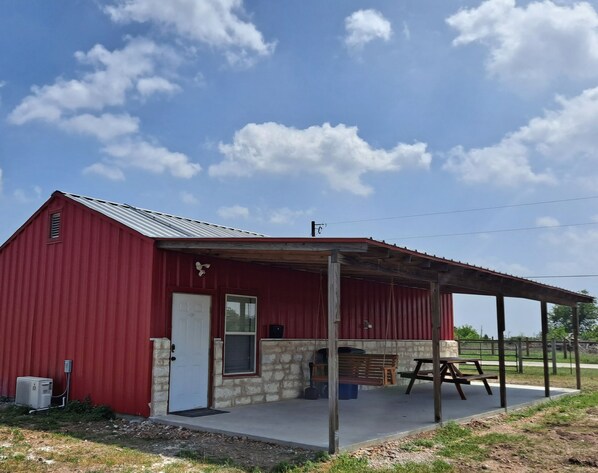A red barn with a covered porch, a white door, and a stone wall.