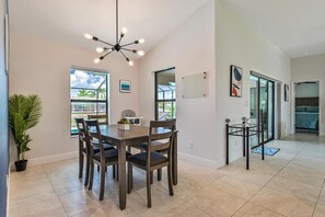 A dining area with a wooden table and chairs, a potted plant, and a modern chandelier.