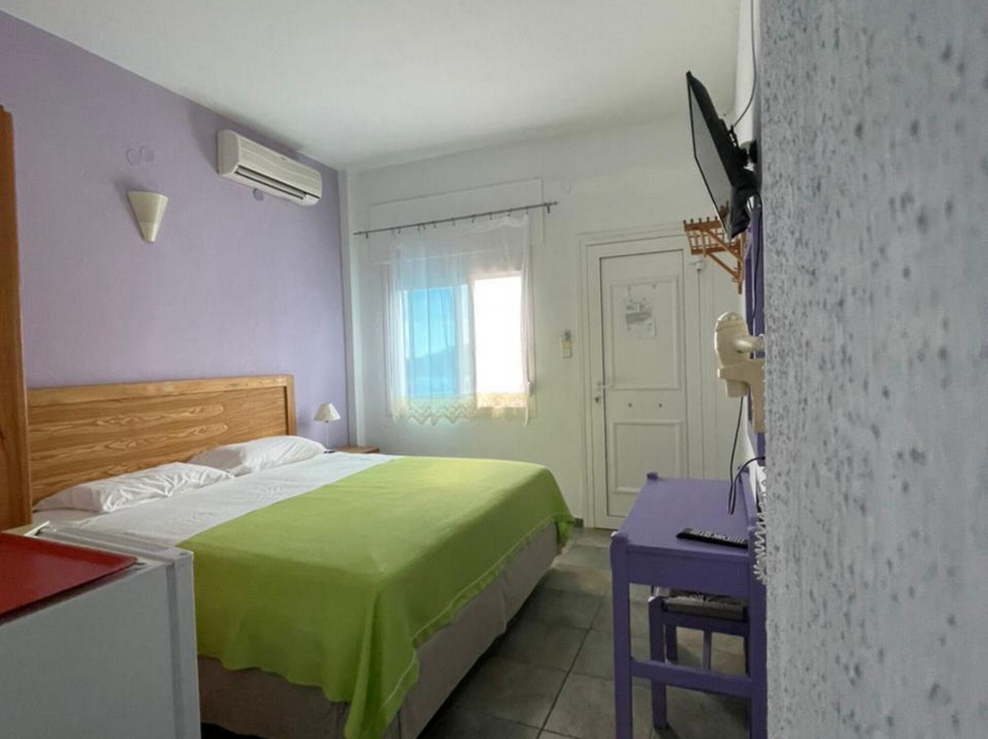 Un dormitorio con cama, escritorio, aire acondicionado, puerta y ventana con cortinas.