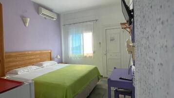 Un dormitorio con cama, escritorio, aire acondicionado, puerta y ventana con cortinas.