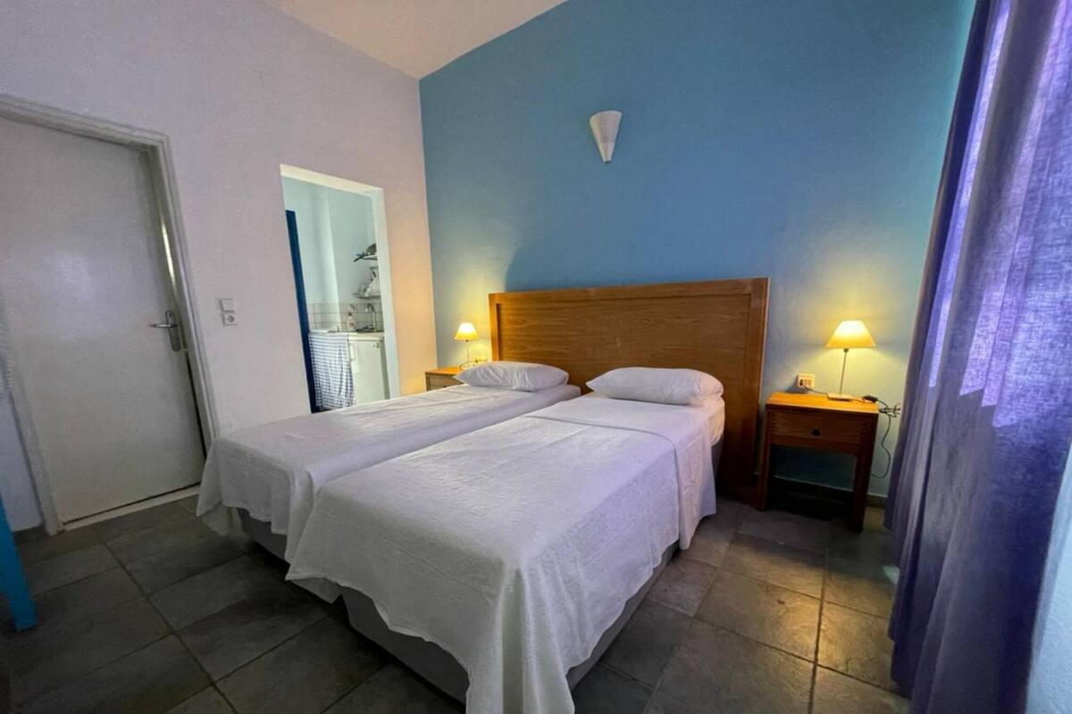 A double bed with white bedding in a room with blue walls, two bedside tables with lamps, and a door to the left.