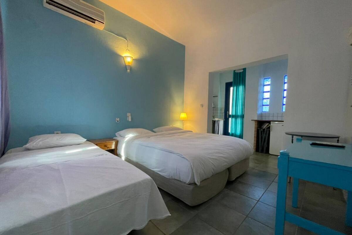 A hotel room with two beds, a small table, a desk, and a bathroom visible through an open door.
