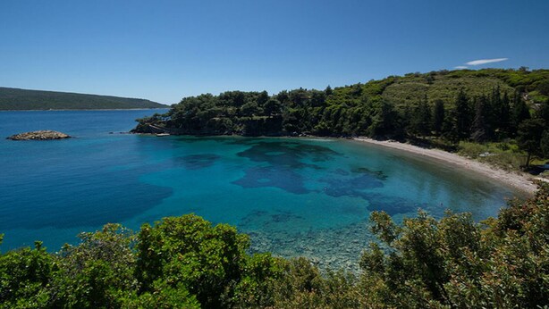 Un paysage côtier caractérisé par une eau turquoise cristalline, une plage de sable et une végétation luxuriante.