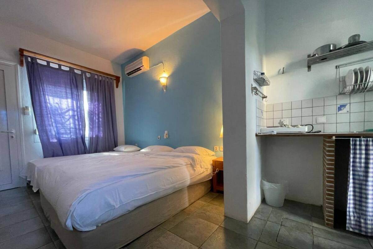 A bedroom with a bed, a nightstand, an air conditioning unit, and a bathroom with a sink and mirror.