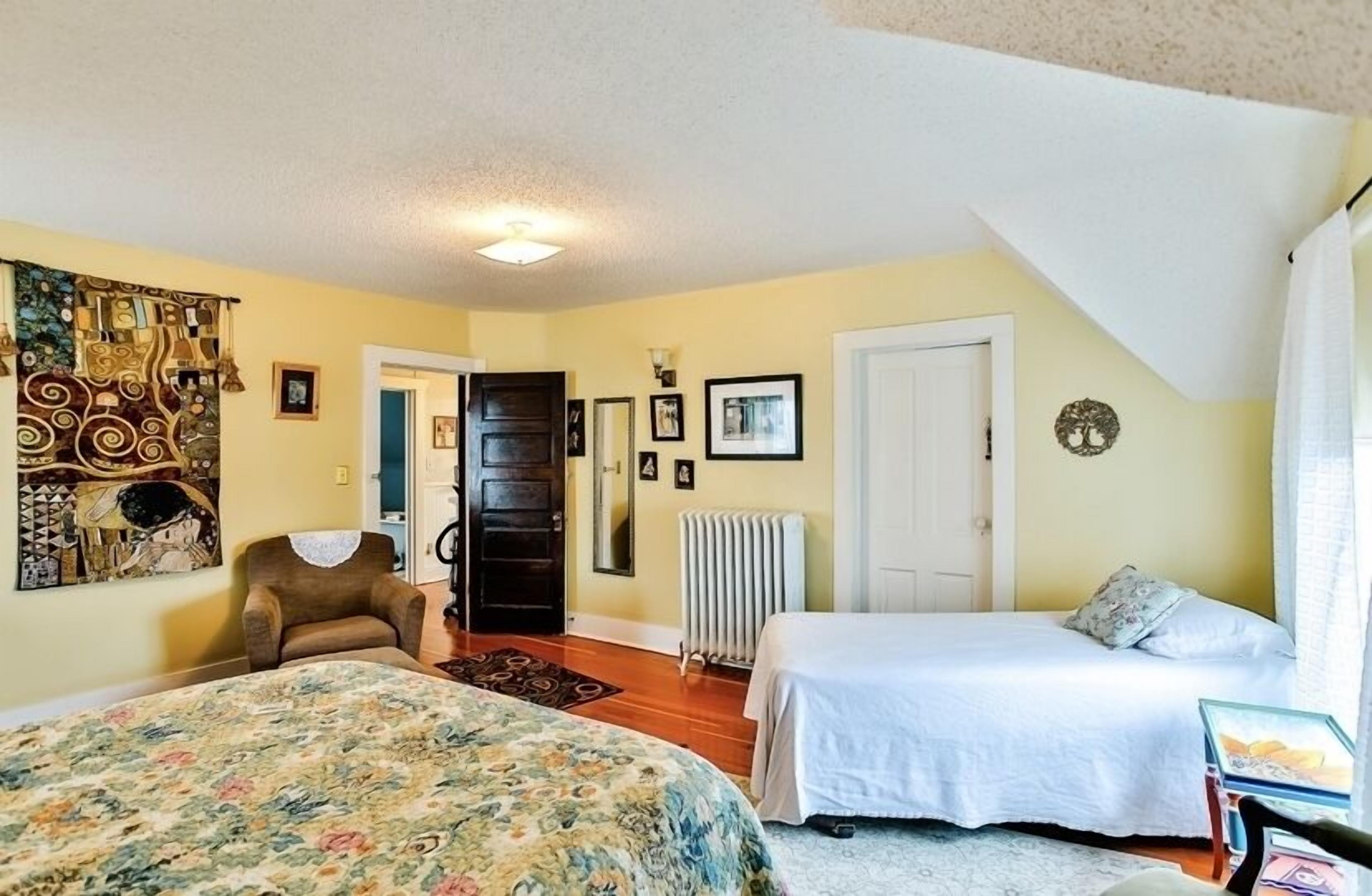 A bedroom with a large bed, a smaller bed, a chair, a radiator, and a door.