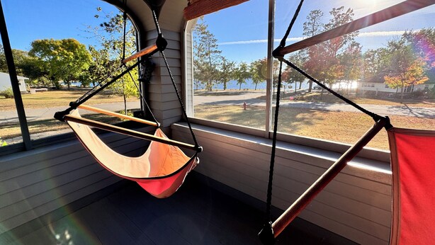 A hammock chair suspended by ropes, a large window with a view of trees and a road, and a wooden floor. - Stately home by Spirit Lake in Menahga (Menahga)