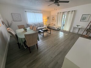 A modern living room with a dining area, a sofa, a coffee table, and a ceiling fan. - Beautiful Quaint 4 plex Heated Pool and Spa Pets Welcome (Naples)