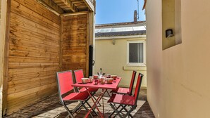 Un mur extérieur en bois, une petite fenêtre et une table avec des chaises et des tasses rouges.