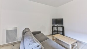 Un salon moderne avec un canapé gris, une table basse en bois et un téléviseur à écran plat posé sur un meuble noir.