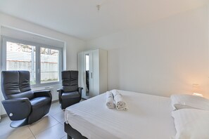 A hotel room with a bed, two chairs, a large window, and a door leading to a balcony.
